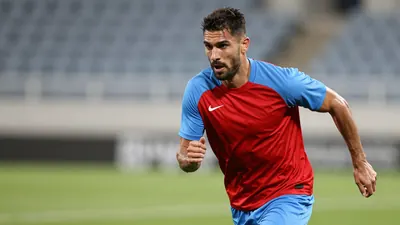 A muscular midfielder in his late 20s, wearing a plain red and sky blue training top with clean fabric texture, sprints...