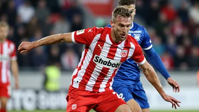A tight action shot of a GIF Sundsvall player in a red and white striped kit, mid-tackle against an Östersunds FK...