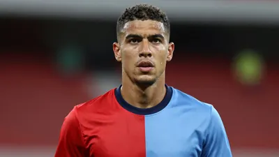 Mid-30s athletic midfielder, intense expression, head-and-shoulders, wearing a plain unmarked training top split red left...