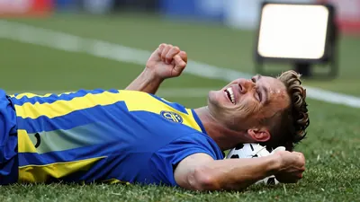 A photorealistic image of an anonymous Gif Sundsvall player lying on the ground with a ball behind his neck, celebrating...