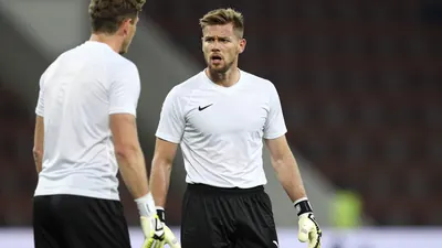 A tight action crop of an anonymous goalkeeper in his mid-20s, with a clean white jersey and black shorts, looking...