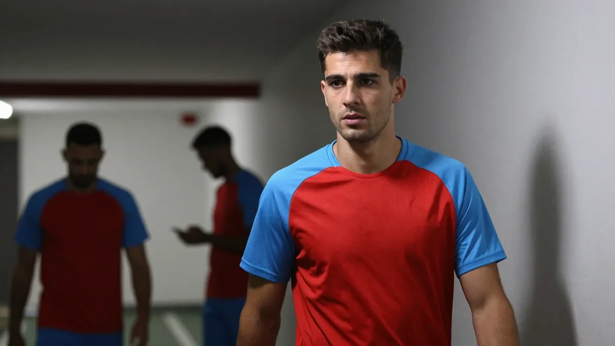 A medium shot of a young, 20-year-old male coach with a fit build, wearing a plain, unmarked red and sky blue training...
