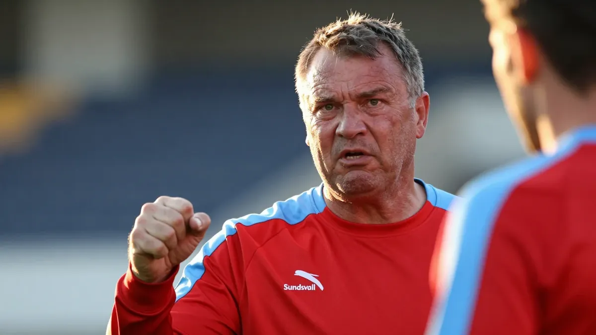 A close-up portrait of a middle-aged, stocky male coach, dressed in a plain red and sky blue GIF Sundsvall training top...